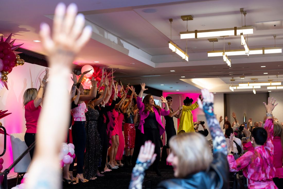 Women on stage with arms raised and drumsticks in hand